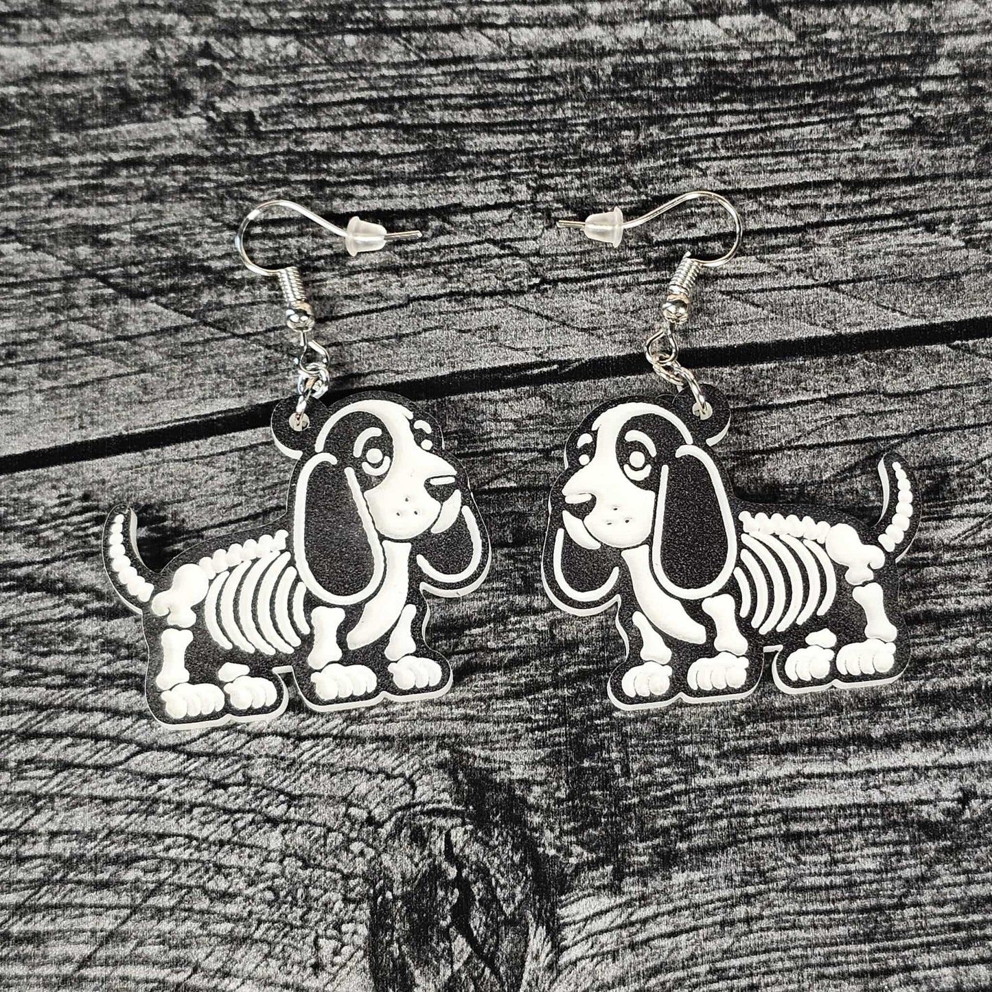 Skeletal Bassett hound dog earrings on a black wooden surface