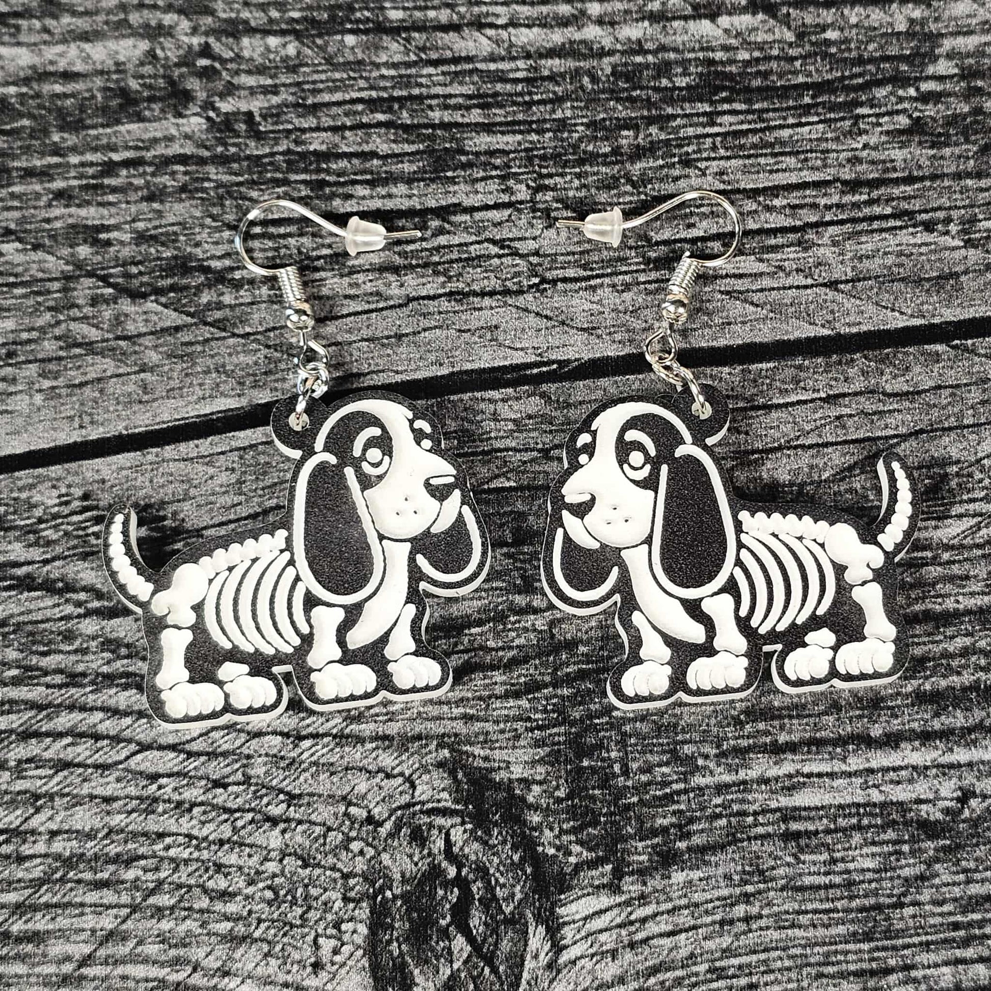Skeletal Bassett hound dog earrings on a black wooden surface