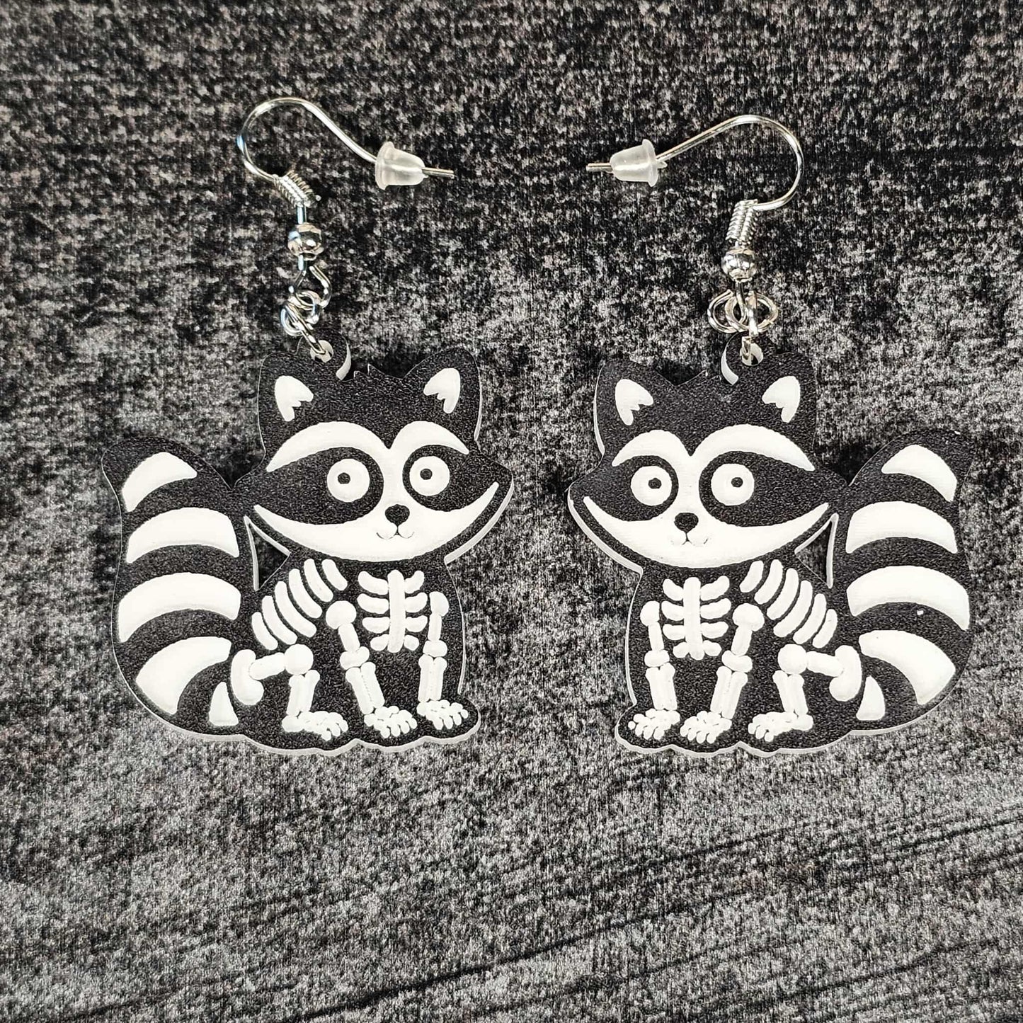Skeletal raccoon earrings on a textured surface