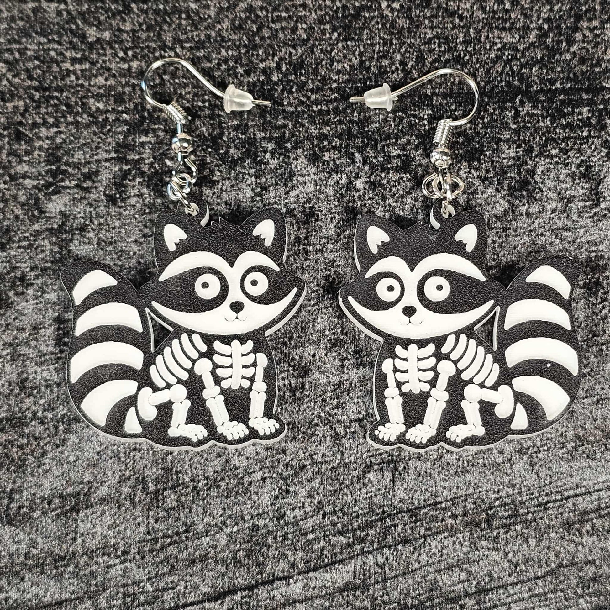 Skeletal raccoon earrings on a textured surface