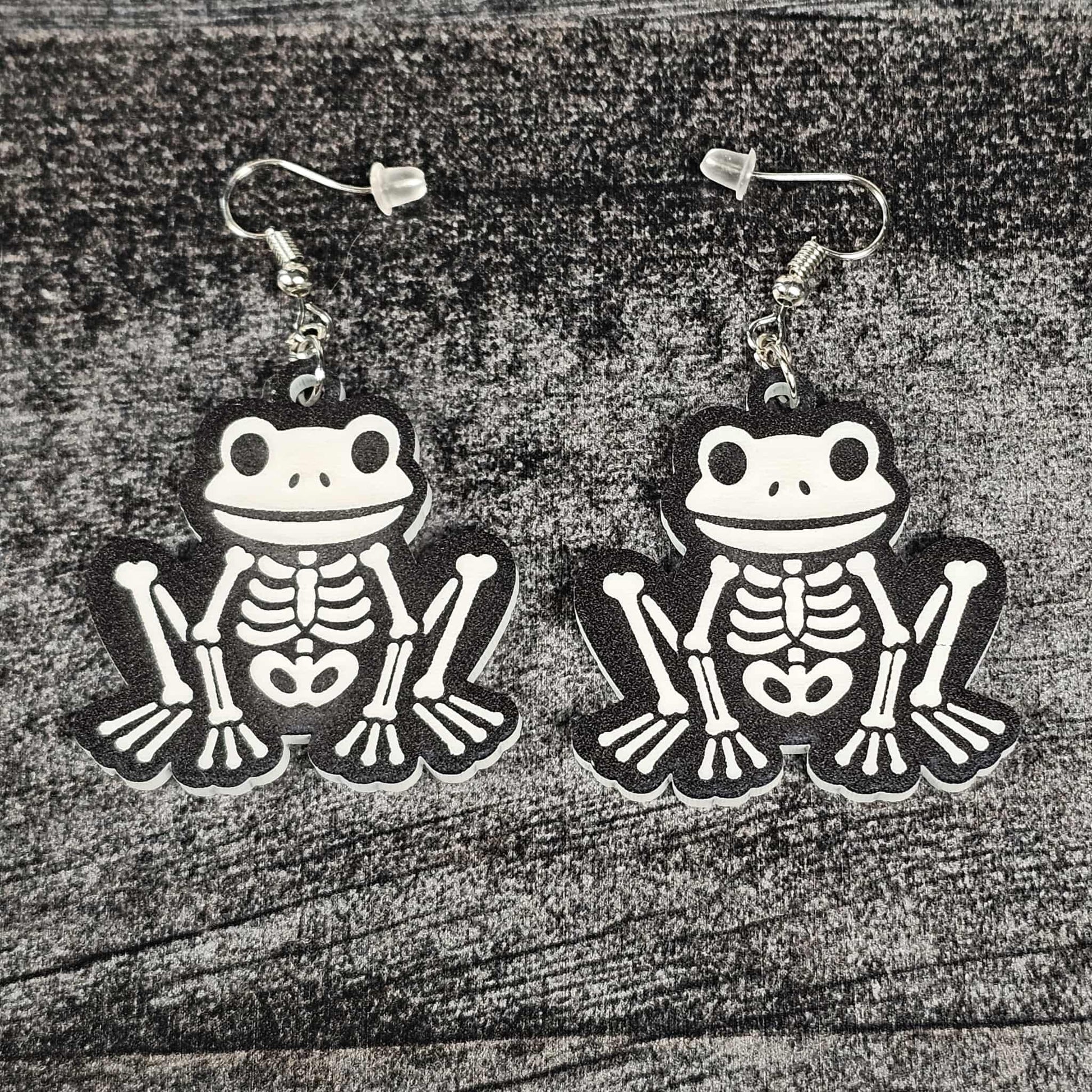 Frog skeleton earrings on a wooden surface