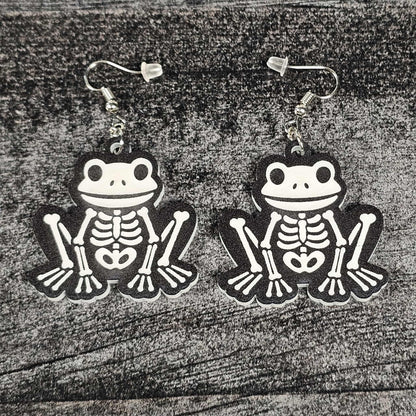 Frog skeleton earrings on a wooden surface
