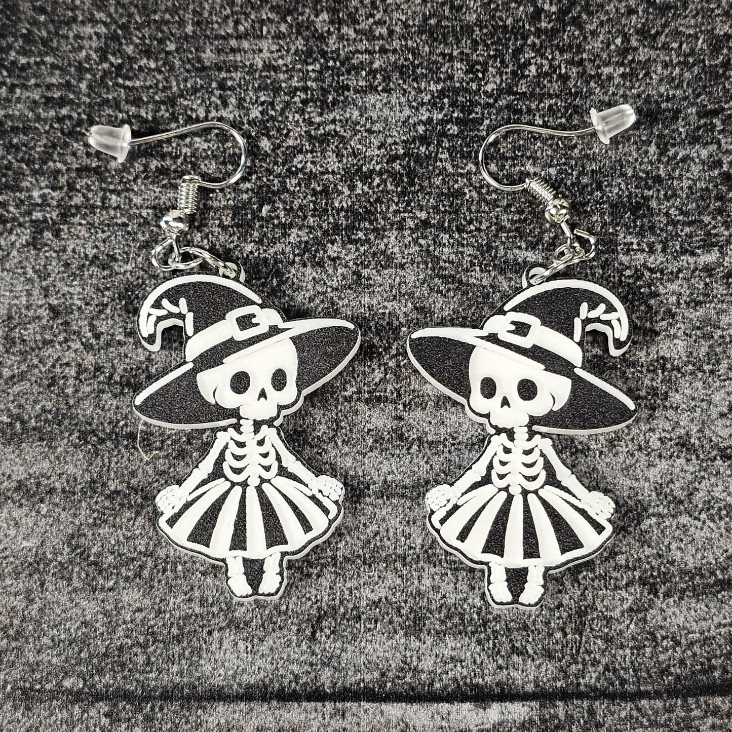 Pair of skeleton witch earrings with hats and dresses on a textured surface