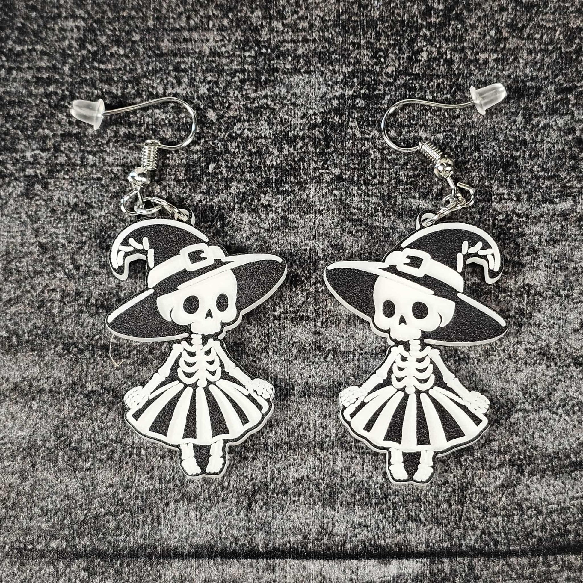 Pair of skeleton witch earrings with hats and dresses on a textured surface