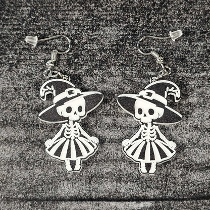 Pair of skeleton witch earrings with hats and dresses on a textured surface