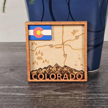 Wooden decorative item with laser-cut map of Colorado and state flag, placed on a wooden surface.