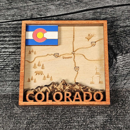 Wooden magnet with laser-cut map of Colorado, state flag, and mountain design on a wooden surface.