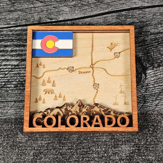 Wooden magnet with laser-cut map of Colorado, state flag, and mountain design on a wooden surface.