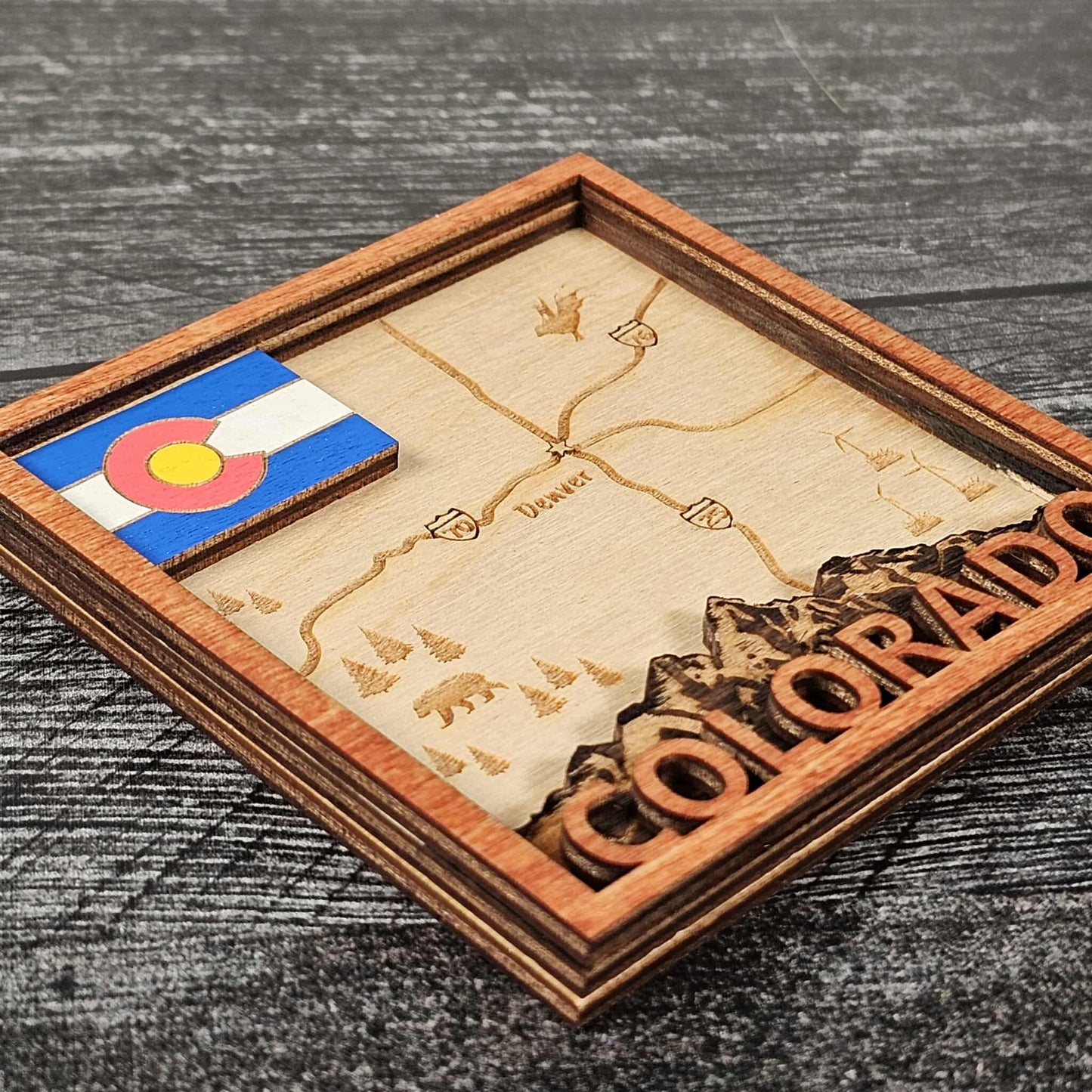 Wooden coaster with Colorado map and flag on a dark surface