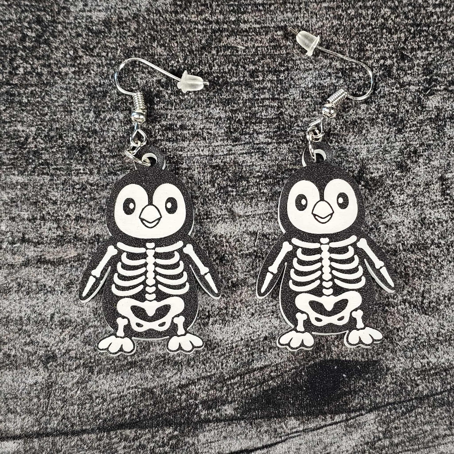 Penguin skeleton earrings on a textured surface