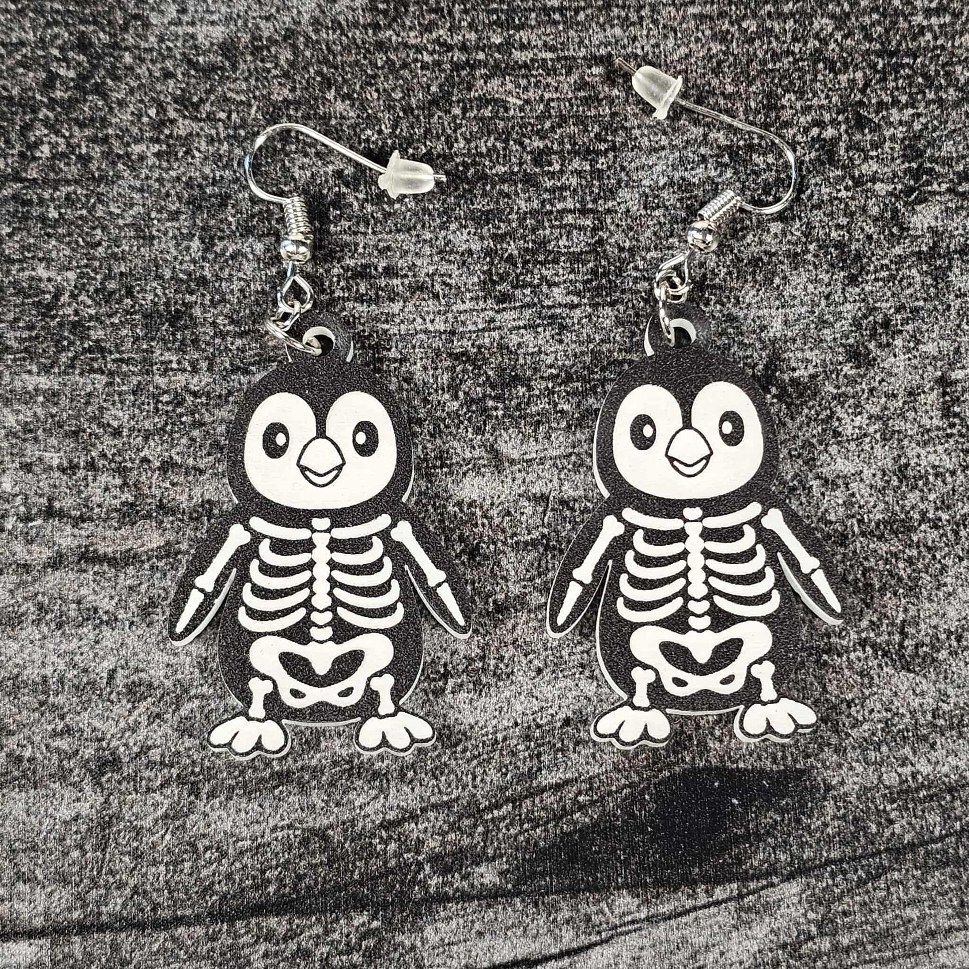 Penguin skeleton earrings on a textured surface