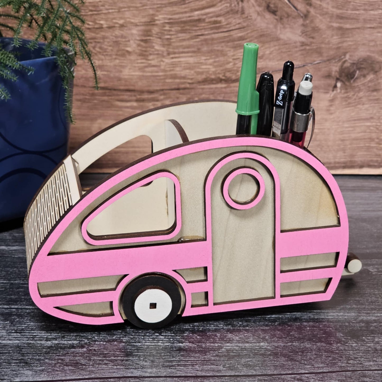 Pink and beige camper-shaped pen holder with markers on a wooden surface