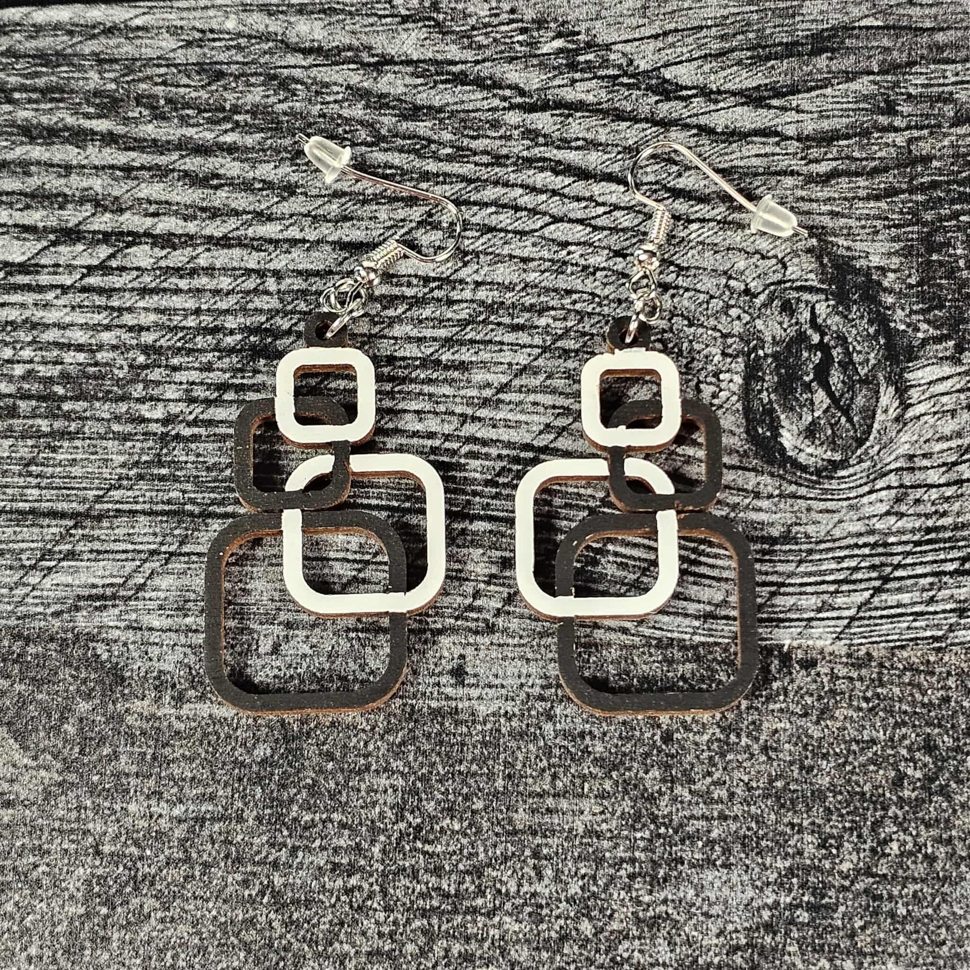 Wooden geometric squares earrings on a textured gray surface.  The four squares of each earring are alternating white and black in color