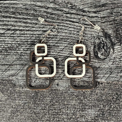 Wooden geometric squares earrings on a textured gray surface.  The four squares of each earring are alternating white and black in color