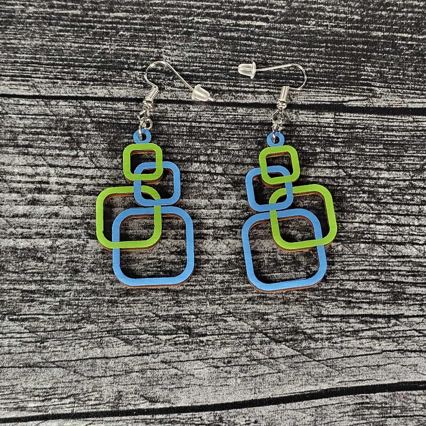 Pair of blue and green square-shaped earrings on a wooden surface.  The squares alternate blue and green.