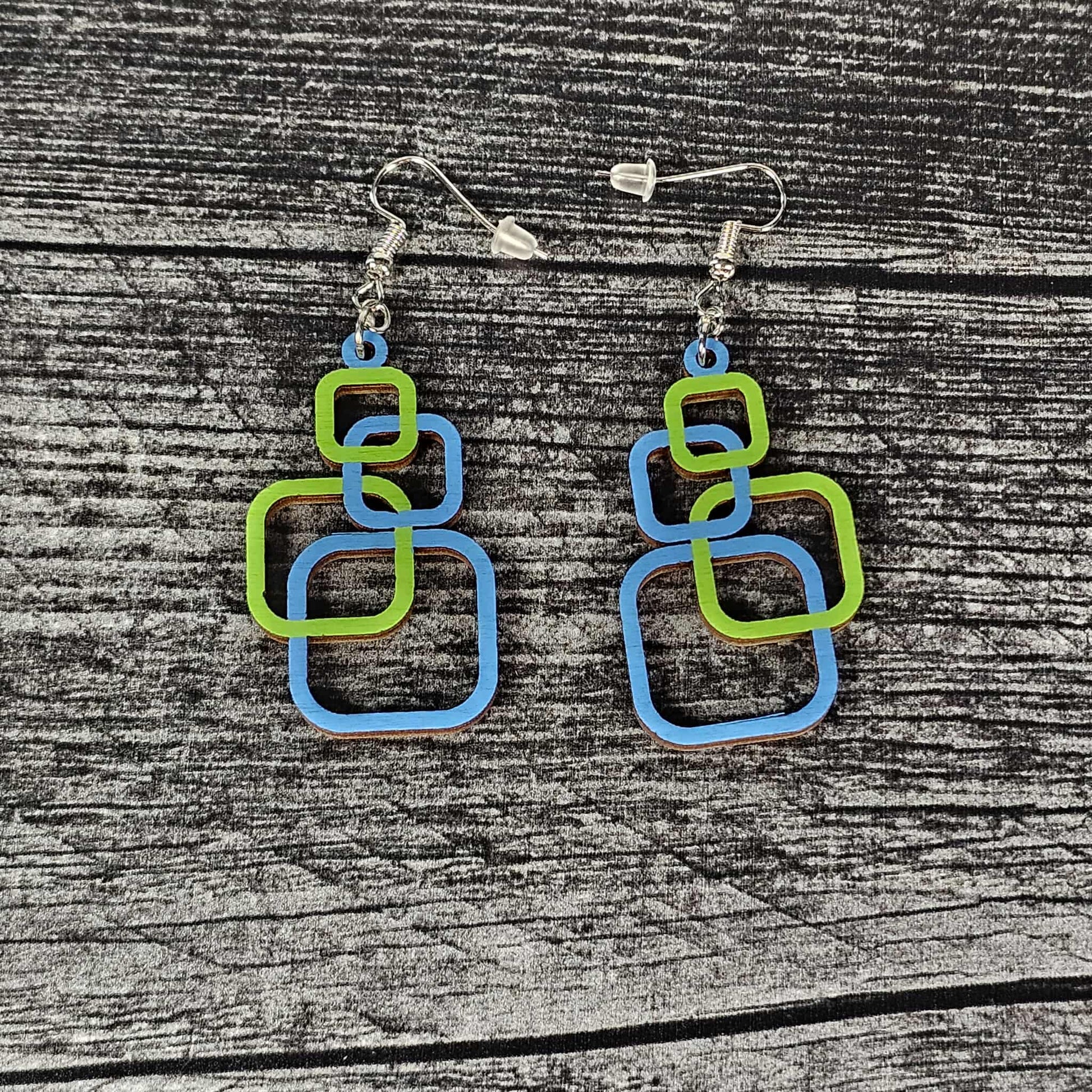 Pair of blue and green square-shaped earrings on a wooden surface.  The squares alternate blue and green.