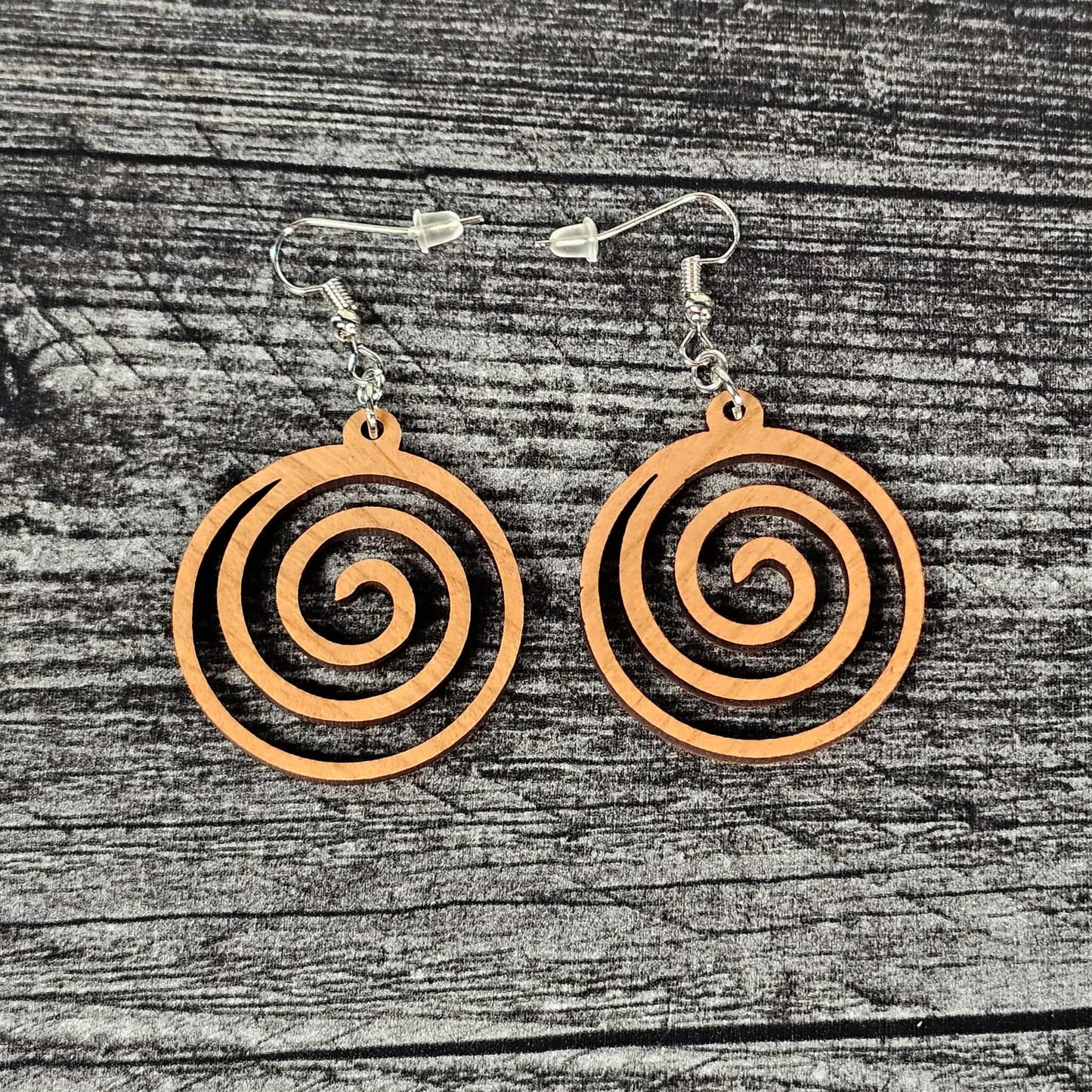 Cherry wood geometric spiral earrings on a wooden surface