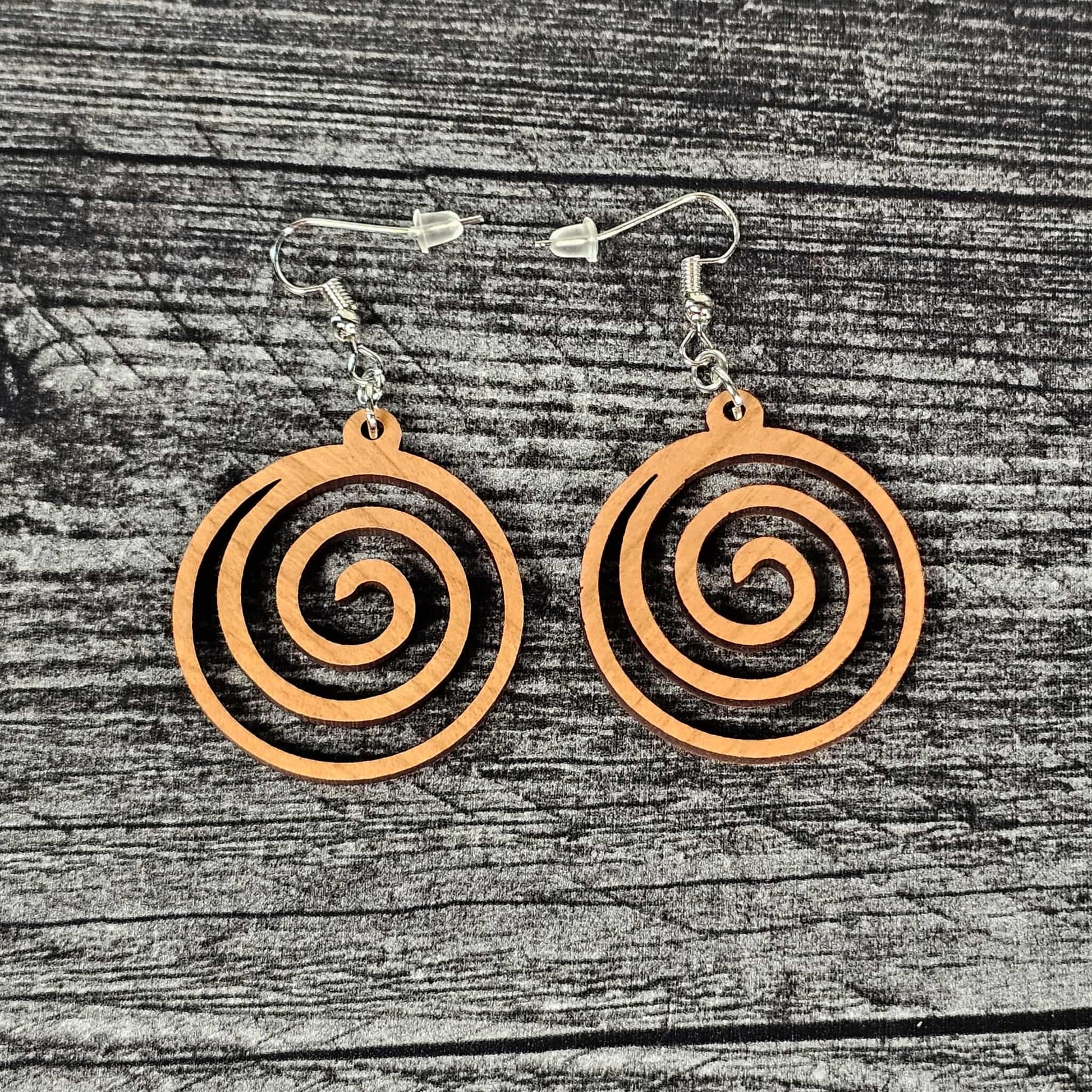 Cherry wood geometric spiral earrings on a wooden surface