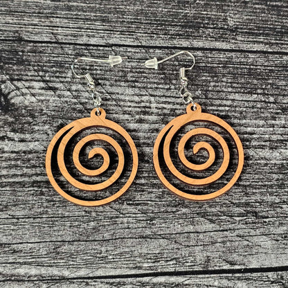 Cherry wood geometric spiral earrings on a wooden surface