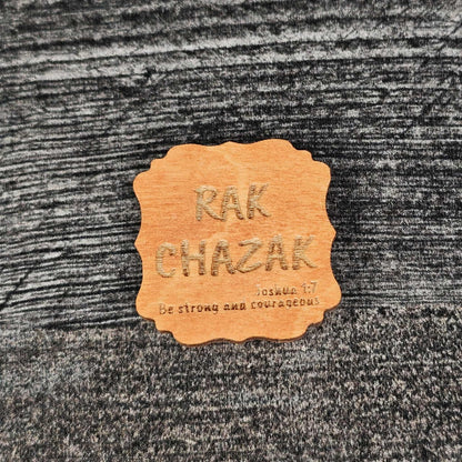 Decorative gunstock stained wooden magnet with 'RAK CHAZAK' text, as well as a quote from Bible verse Joshua 1:7 on a textured surface.
