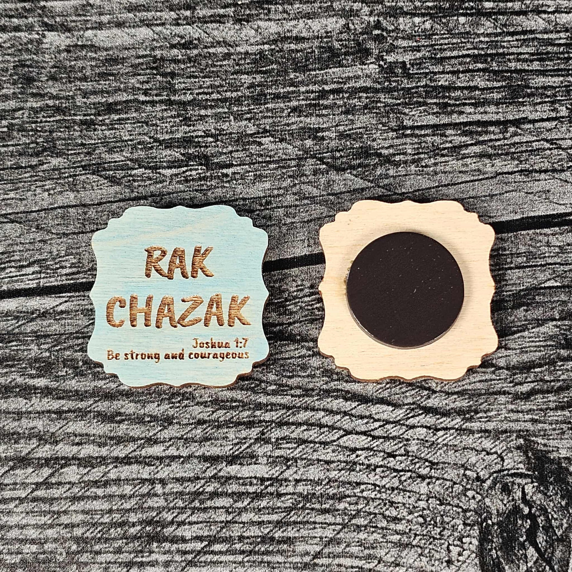 Decorative blue stained wooden magnet with 'RAK CHAZAK' text, as well as a quote from Bible verse Joshua 1:7 on a textured surface.  The back of the magnet is also shown.