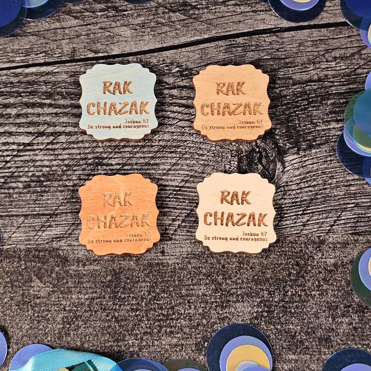 Four 'Rak Chazak' magnets on a wooden surface with colorful circular objects around.  Each of the four color options are shown (blue, walnut, gunstock, and unstained)