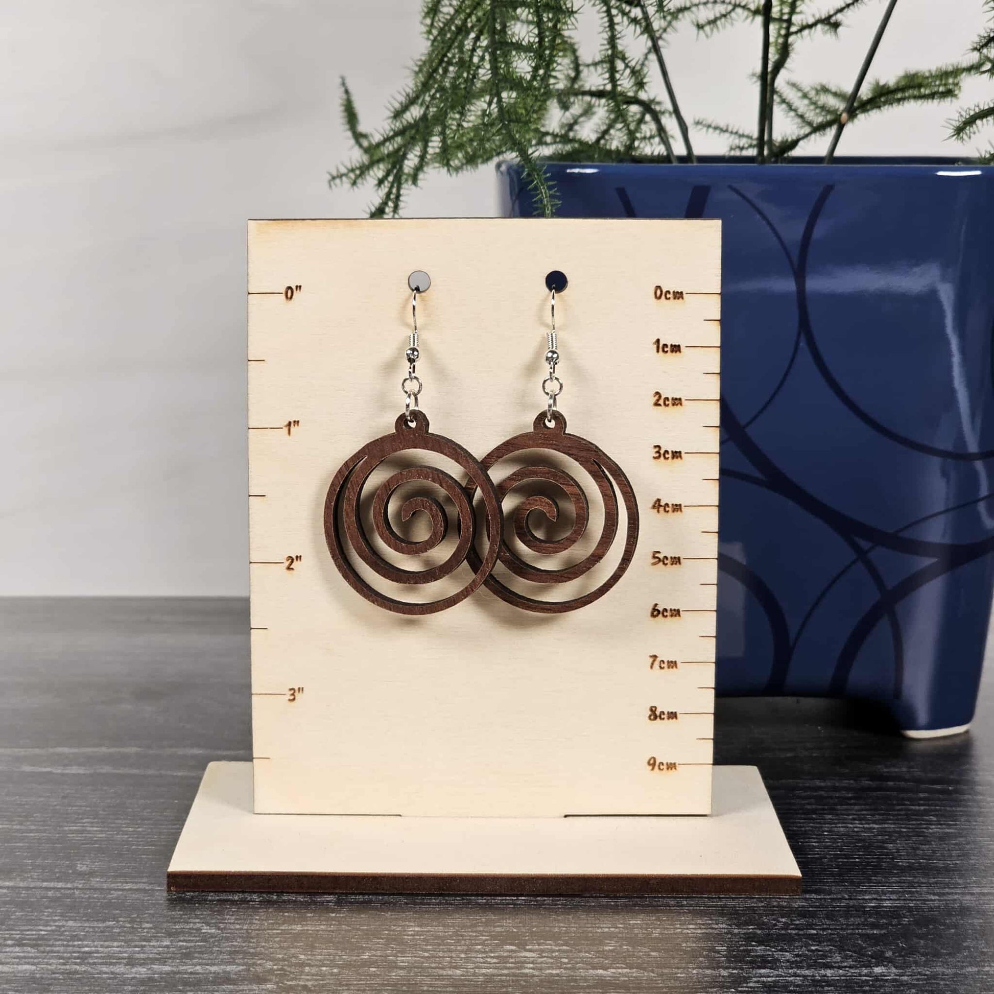 Pair of walnut spiral earrings on a measurement card with a blue vase in the background