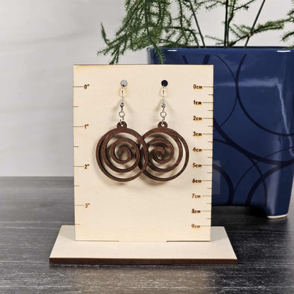 Pair of walnut spiral earrings on a measurement card with a blue vase in the background