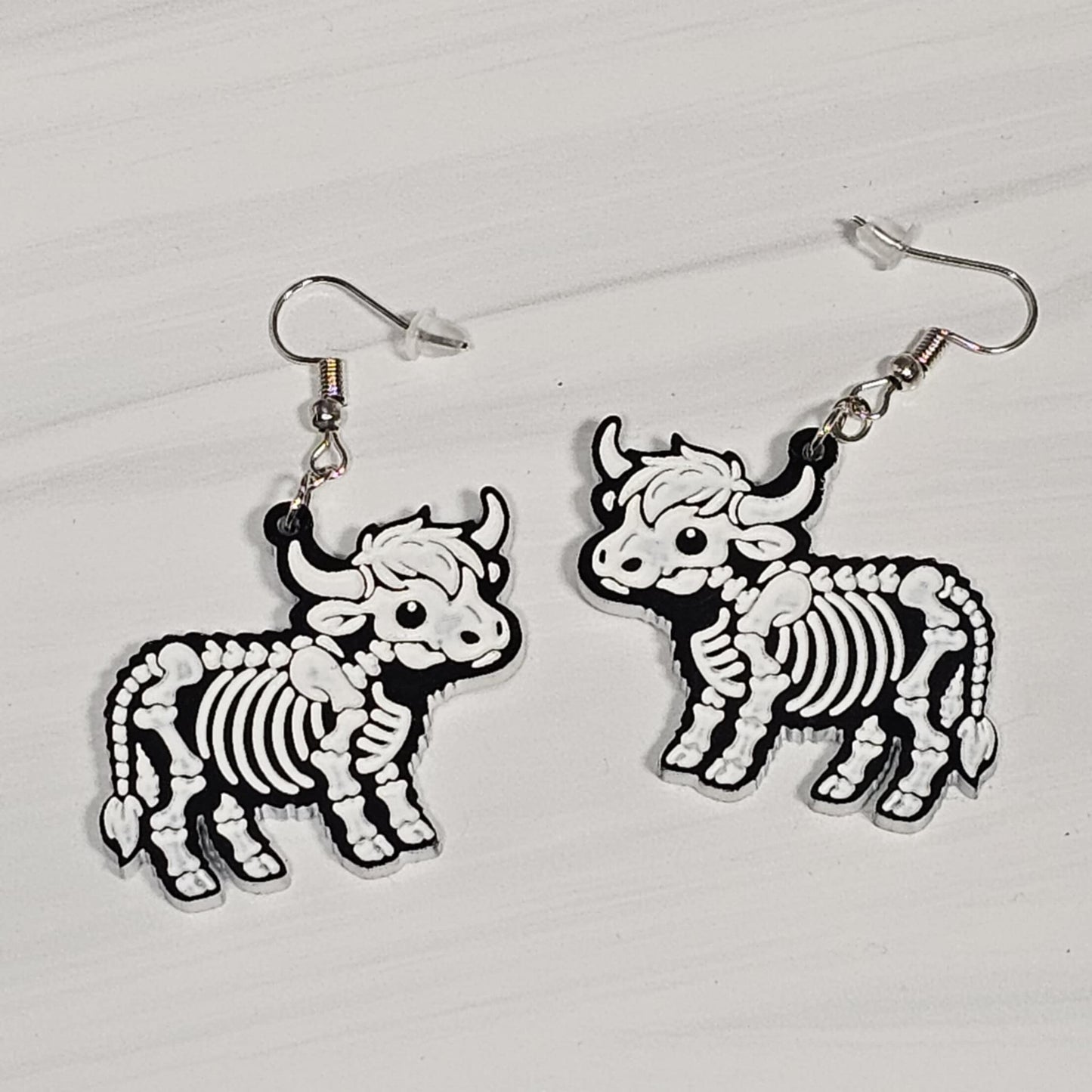 Highland Cow skeleton design earrings on a light gray background