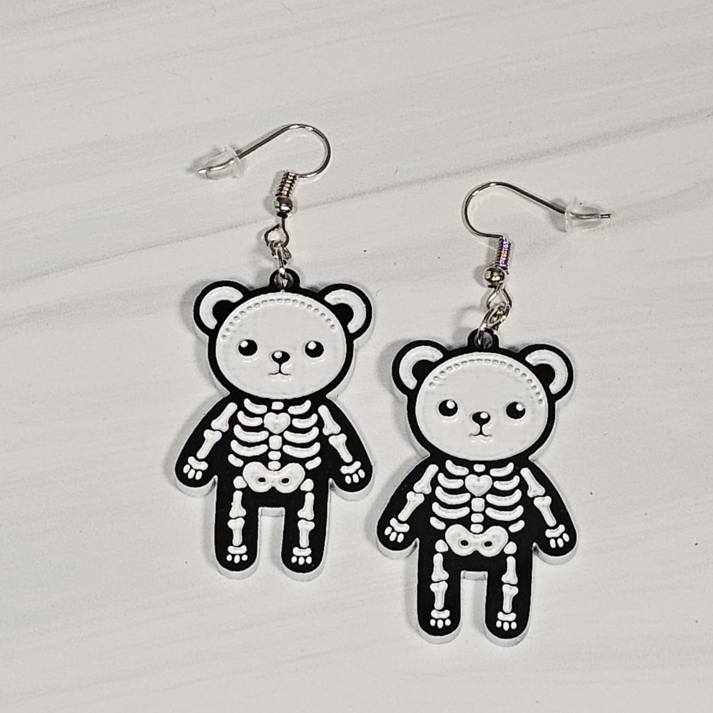 Pair of skeleton teddy bear earrings on a light gray background