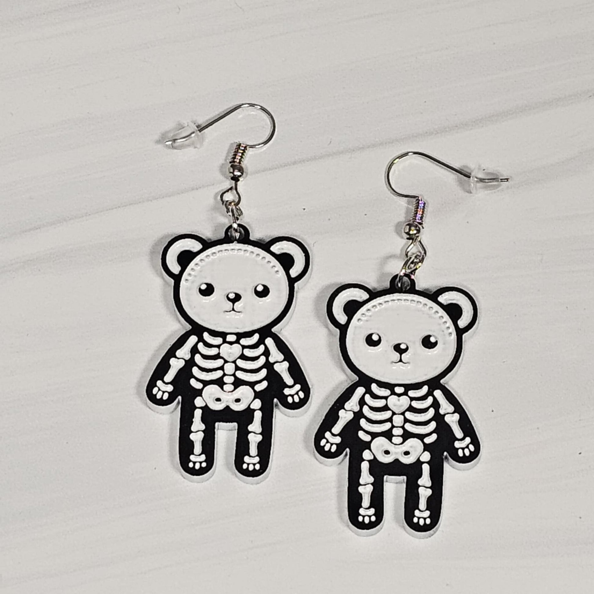 Pair of skeleton teddy bear earrings on a light gray background