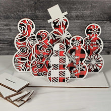Load image into Gallery viewer, Decorative wooden cutout with red and black buffalo plaid color and white snowflake patterns on a wooden surface.