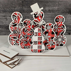 Decorative wooden cutout with red and black buffalo plaid color and white snowflake patterns on a wooden surface.