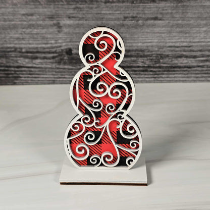 Decorative wooden figure with red and black buffalo plaid pattern topped with a swirls design in white standing on a white surface and gray background