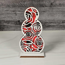 Load image into Gallery viewer, Decorative wooden snowman sculpture with red and black buffalo plaid pattern topped with swirly rose design in white 