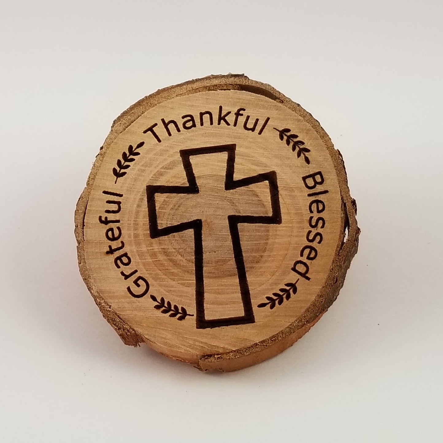 A wooden cookie with 'Thankful' and 'Blessed' text around a central cross design, on a white background.
