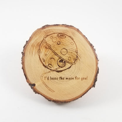 Wooden slice with moon engraving and text 'I'd lasso the moon for you!' on a white background