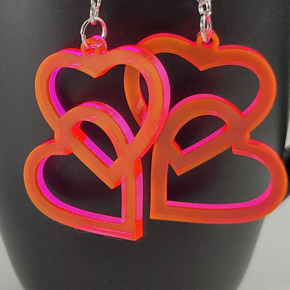 Neon pink heart-shaped earrings on a black background