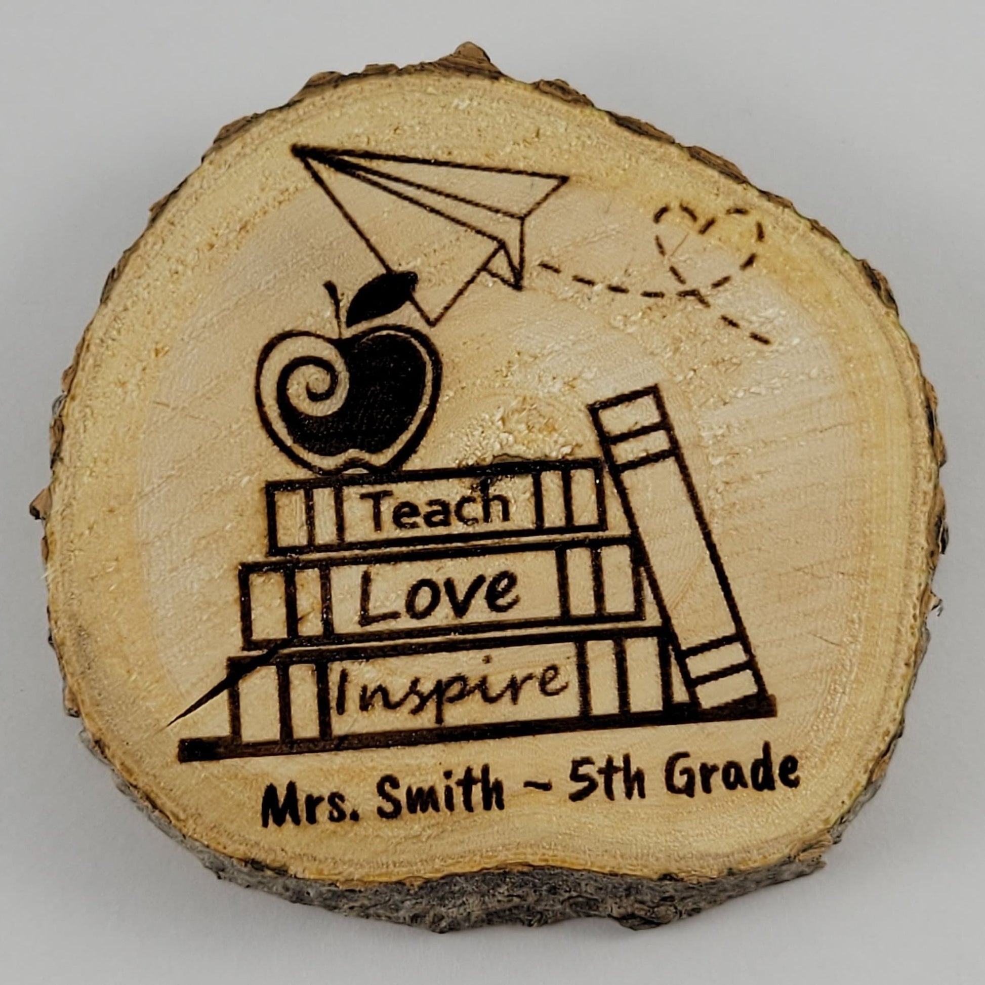 A wooden magnet with a teacher's name and the phrase 'Teach Love Inspire' along with an illustration of a kite and books.