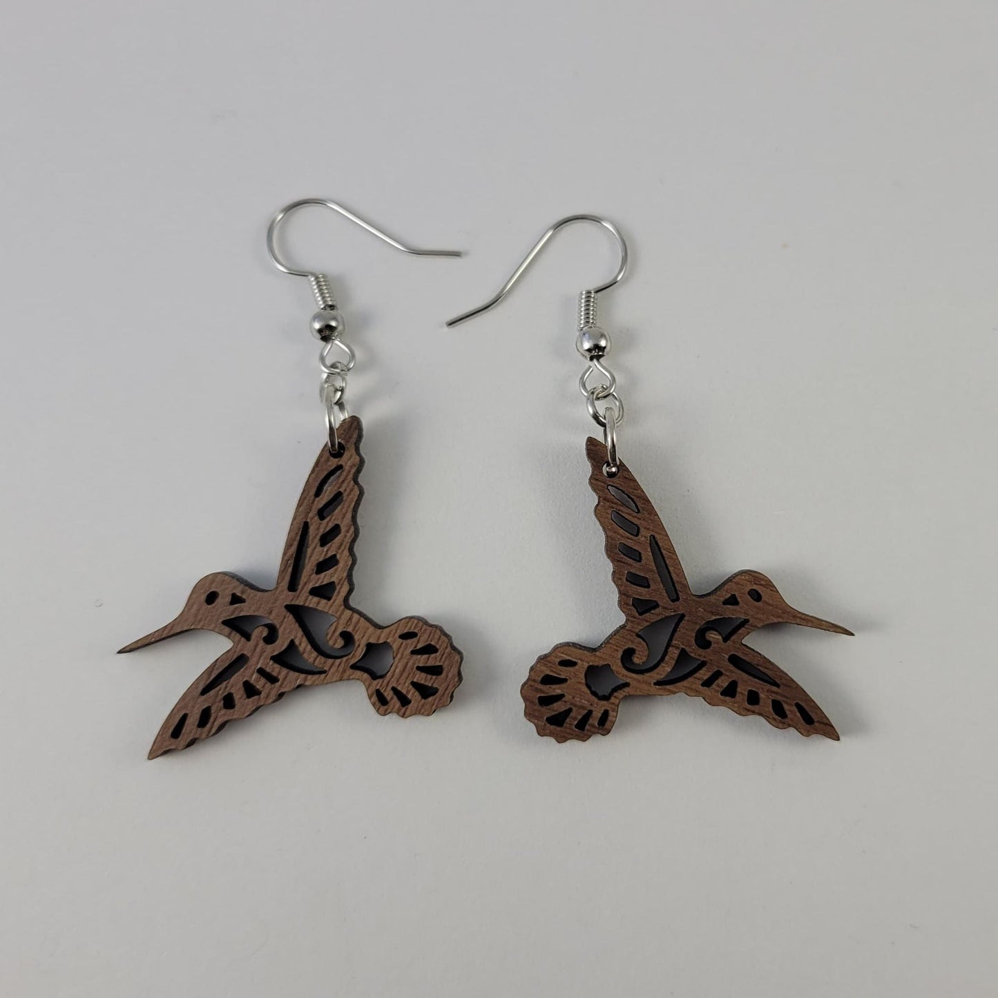 A pair of brown walnut hummingbird earrings with silver fish hooks and silicone backing.