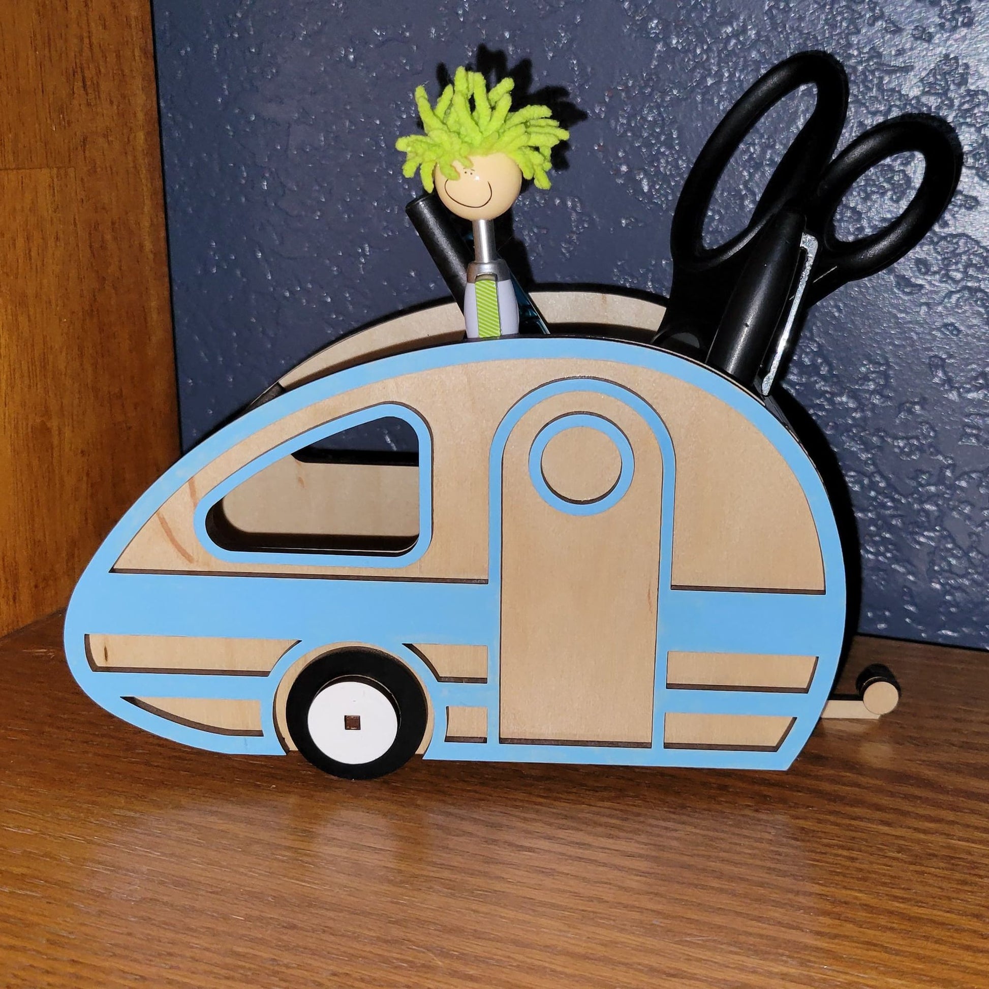 Desk organizer shaped like a camper with stationery items on a wooden surface.