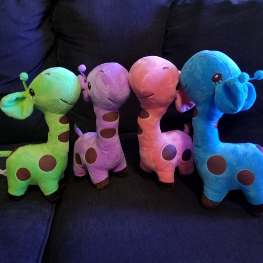 A set of four plush giraffe toys in different colors placed on a couch, with a focus on their cute and friendly design.
