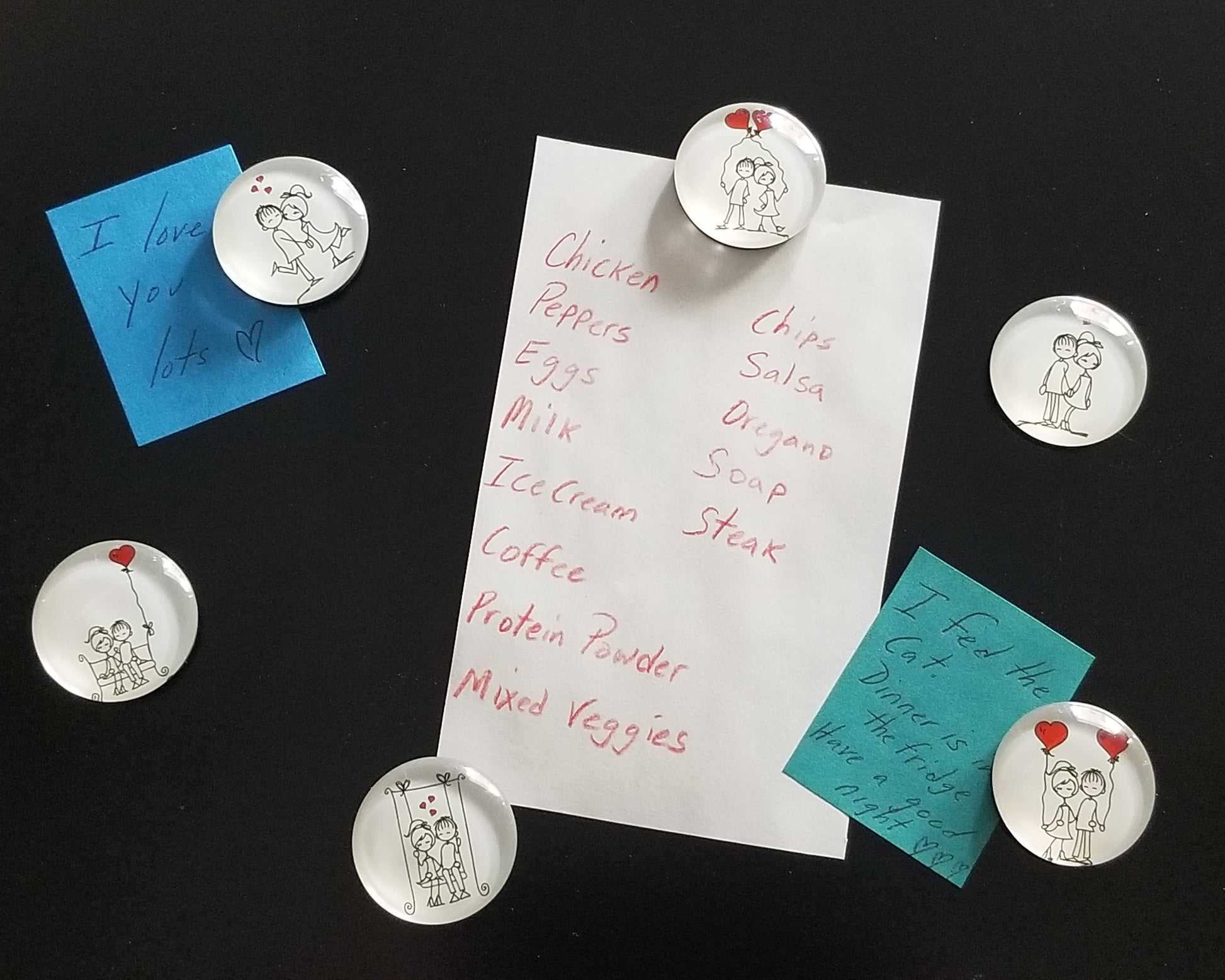 Small round magnets with couple and heart designs on a piece of paper with handwritten text.