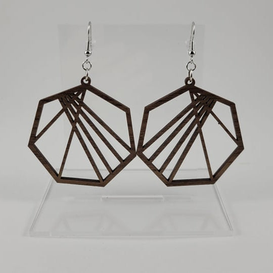 A pair of brown geometric heptagon earrings made of walnut wood, with silver fish hook settings and a silicone backing, displayed on a clear stand.
